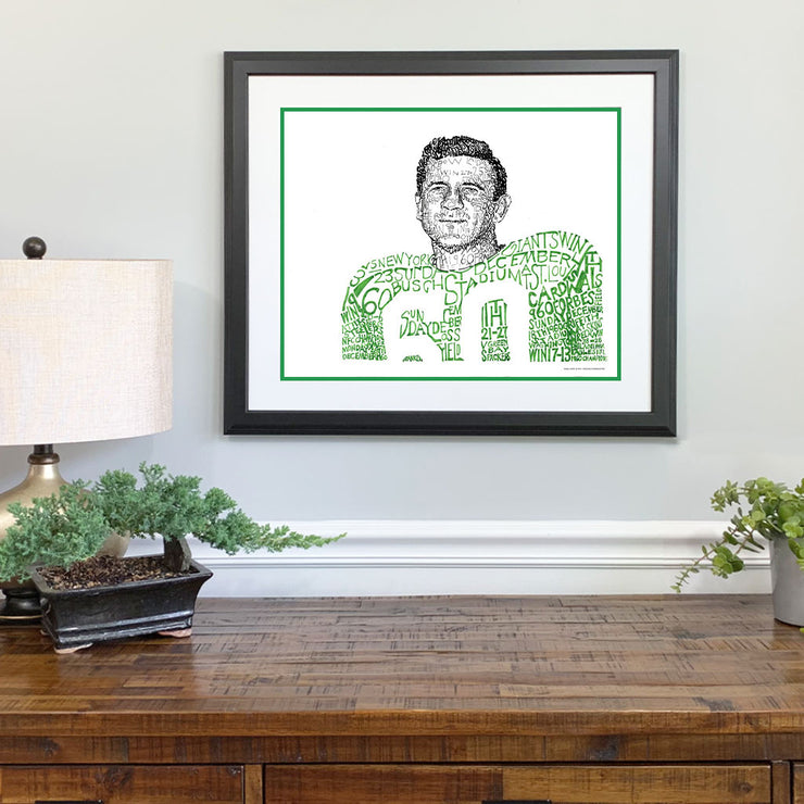 Matted and framed wall word art print of 1960 Philadelphia Eagle Chuck Bednarik hangs on wall over wooden table.