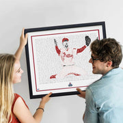 Woman and man smile while hanging framed handwritten word art portrait of Brad Lidge celebrating last out in 2008 World Series.