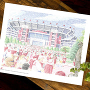 Unframed word art print of Bryant Denny Stadium in Alabama lies flat on wood table next to plant.