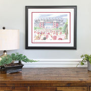Matted and framed word art print of Bryant Denny Stadium in Alabama hangs on wall above wooden table.