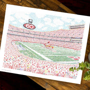  Unframed word art print of fans and field at Kansas City Chiefs’ Arrowhead Stadium lies flat on wooden table.