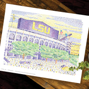  Purple and yellow LSU Tiger artwork of LSU stadium and green trees comprised of words on wood table.