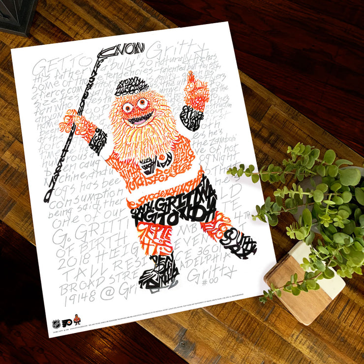 Unframed print of word art portrait of Gritty, Philadelphia Flyers mascot, lies flat on wooden table next to small plant.