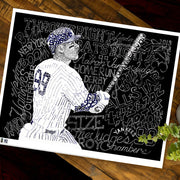 Unframed word art Aaron Judge poster lies flat on wooden table next to small plant.