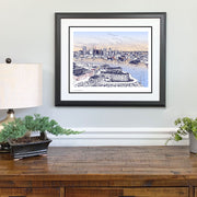 Matted and framed word Baltimore skyline art print hangs on wall above wooden table.