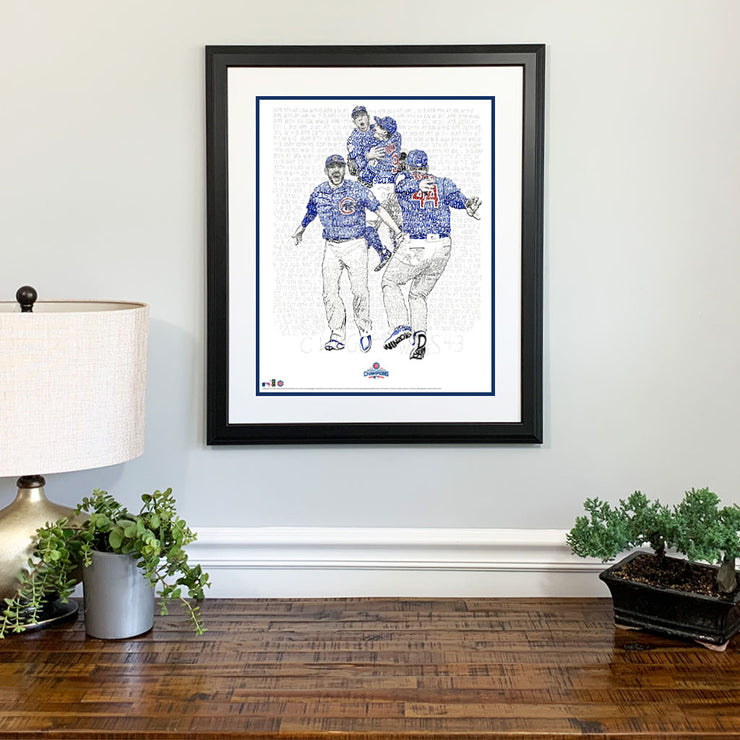 Matted and framed wall word art print depicting 2016 Chicago Cubs World Series win hangs on wall over wooden table.