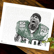 Unframed word art print of Philadelphia Eagles’ Brian Dawkins lies flat on wooden table next to small plant.