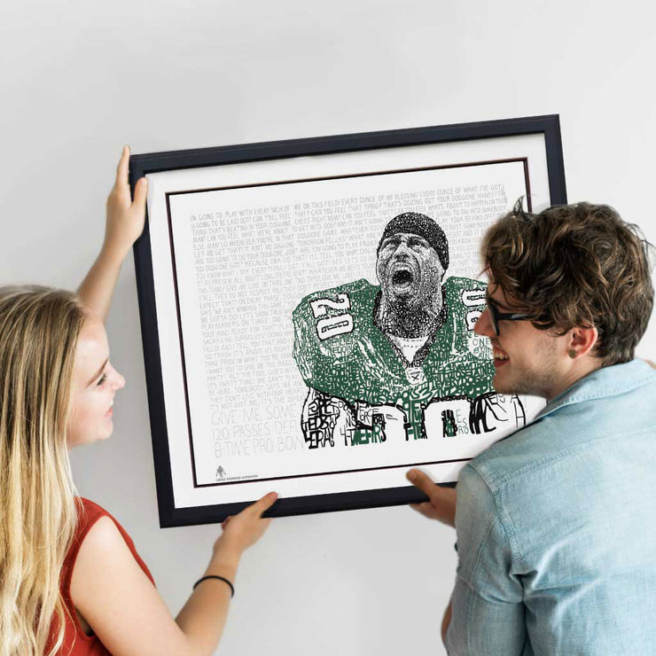 Woman and man smile as they hang framed word art portrait of Philadelphia Eagles’ Brian Dawkins on wall.