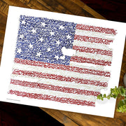 Unframed print of American flag art—handwritten National Anthem lyrics forming flag image—lies flat on wood table.