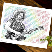 Unframed print of Jerry Garcia art, portrait handwritten from lyrics of three of his songs, lies flat on wooden table.