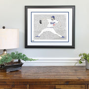 Matted and framed piece of LA Dodgers wall art, a word art portrait of pitcher Clayton Kershaw, hangs above wooden table.