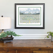 Matted and framed word art print of Lambeau Field, one of the best Green Bay Packers gifts, hangs on wall above wood table.