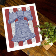 Unframed print of Liberty Bell art, handwritten with the text of the Declaration of Independence, lies flat on wooden table.