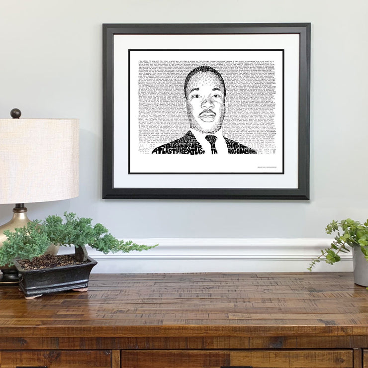 Black and white Martin Luther King Jr. artwork of portrait made of hand-written words on wall above wood desk.