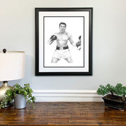Framed Muhammad Ali art in black and white made of small hand-written words from his famous speeches above wood dresser.