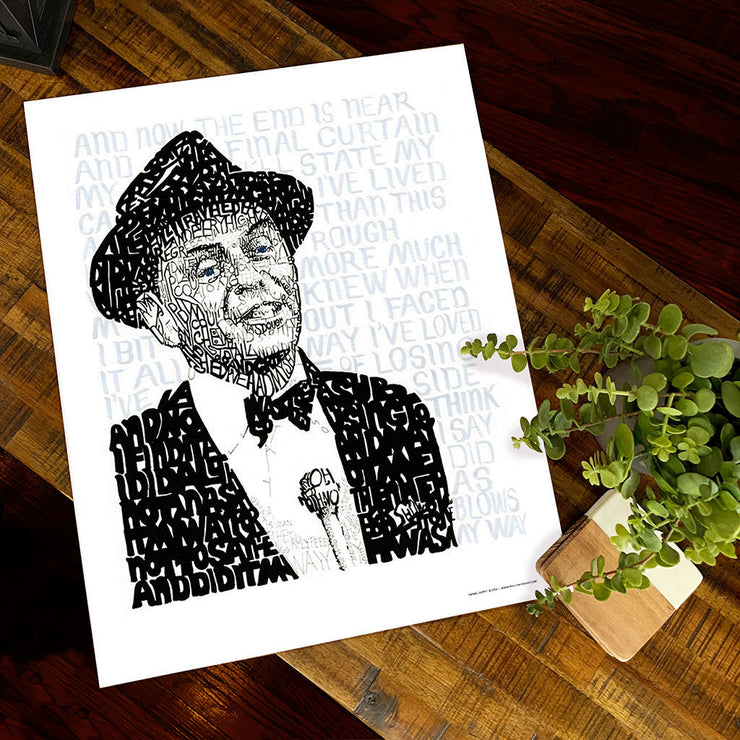 Unframed print of Frank Sinatra art, his portrait handwritten with the lyrics to “My Way,” lies flat on wooden table.