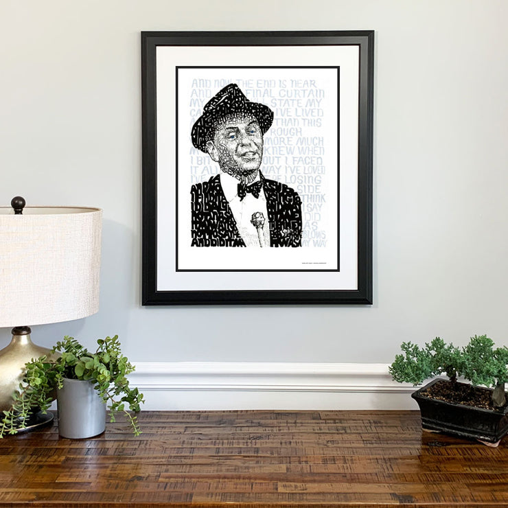 Matted and framed word art portrait of Frank Sinatra hangs on wall over wooden table, one of the best Frank Sinatra gifts.